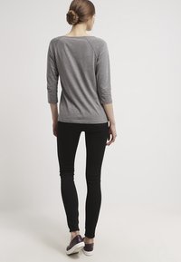 Graues Oberteil mit dreiviertel Ärmeln, eng anliegende schwarze Leggings und dunkle Schuhe; glatter Stoff mit einfachem Design, ohne Muster oder Verzierungen.