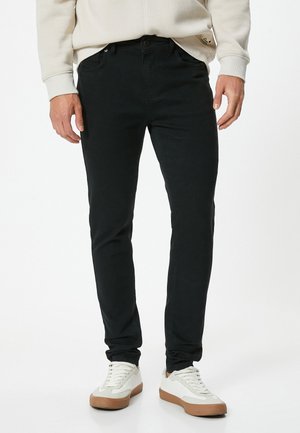 Jeans slim fit noirs avec une texture lisse et des coutures de poches subtiles, associés à des baskets basses blanches et beiges.