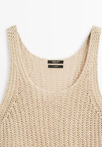 Beige linned-top med løs strikketekstur, med brede skulderstropper og rundet halsudskæring, synligt mærke bagpå.