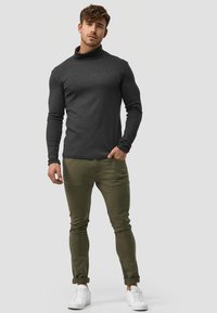 Ciemnoszary sweter z golfem i długimi rękawami, zestawiony z oliwkowozielonymi spodniami slim-fit i białymi trampkami. Prosty, casualowy design.