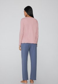 Conjunto de loungewear de dos piezas con una parte superior rosa y pantalones azules. La parte superior presenta un escote redondeado y un dobladillo con forma de concha, mientras que los pantalones tienen un corte holgado.