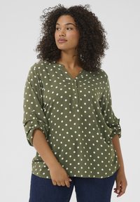 Roheline polka dot mustriga pluus V-kaelusega ja nööbidetailidega. Omab rullitud varrukat ja lõdva siluetti, valmistatud kergest kangast.