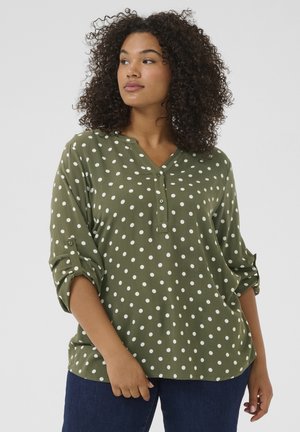Blouse verte à pois avec un décolleté en V et des détails de boutons. Dotée de manches retroussées et d'une coupe loose, fabriquée dans un tissu léger.