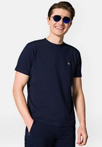 Granatowa koszulka z krótkim rękawem wykonana z bawełny, z okrągłym dekoltem i małym białym logo po lewej stronie klatki piersiowej.