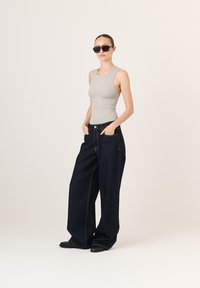 Heled hall ribaga tank top koos kõrge vöökoht ja tumepunased laiad teksapüksid. Mustad ruudukujulised prillid. Mustad tekstureeritud tasased kingad.