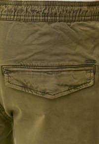 Olivgrüne Stretch-Baumwollhose mit einem gerafften Bund, einer flachen Gesäßtasche und Ziernähten.