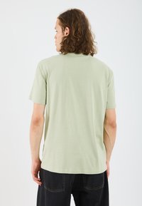 Light green short-sleeve t-shirt with a relaxed fit, smooth texture, rounded neckline, and a straight hem, worn with dark jeans.