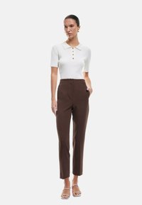 Witte geribde polo met korte mouwen, met een kraag en knoopdetails, gecombineerd met high-waisted bruine broeken met een rechte pasvorm.