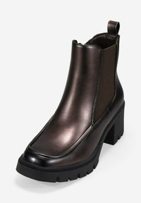 Botín de cuero negro brillante hasta el tobillo con tacón grueso, paneles laterales elásticos, tirador en la parte posterior y suela gruesa con agarre.