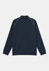 Námořnicky modrá sportovní bunda s vysokým límcem, dlouhými rukávy a bílými linkami podél ramen a švů. Hladká, lehká látka.