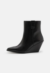 Bottine noire en cuir avec un bout pointu et un talon compensé. Présente une texture lisse avec un onglet latéral et des détails de couture.
