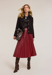 Giacca nera con bottoni dorati, top di satin, gonna plissettata in pelle bordeaux e stivali al ginocchio in stampa pitone marrone. Inclusa borsa grigia.