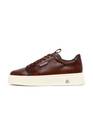 Lage bruine leren sneaker met bijpassende veters, witte dikke rubberen zool en een trek-lusje op de hiel tegen een witte achtergrond.