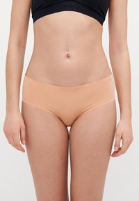 Nude krāsas bezšuvīgas puiša šortus, kas izgatavoti no mīksta auduma, ar gludu stiept dizainu un minimālistisku jostas daļu ar smalku zīmola detaļu.