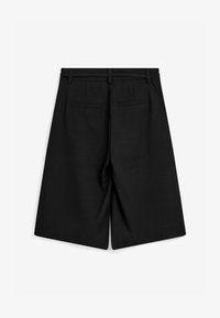 Pantalones cortos a medida de largo hasta la rodilla en negro con presillas para cinturón y dos bolsillos de ojal en la parte trasera, mostrados desde atrás sobre un fondo blanco.