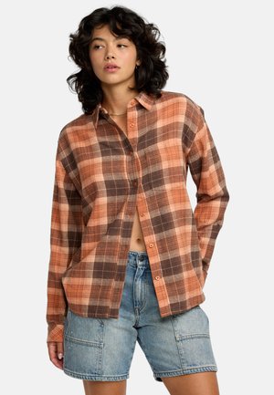 Plaid shirt in orange, brown, and beige tones, made of textured fabric, featuring a button-down front and relaxed fit. Paired with denim shorts.