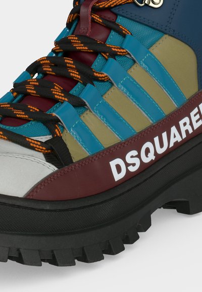 Gros plan d'une chaussure de randonnée multicolore avec des lacets noirs à rayures orange, des panneaux bleus et beiges, une bordure bordeaux et « DSQUARED » en blanc sur le bord de la semelle.