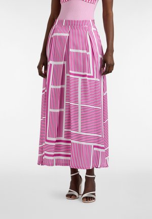 Vrouw draagt een midi-rok met roze en witte geometrische print met plooien en witte sandalen met hoge hakken en bandjes, weergegeven van taille tot beneden.