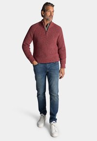 Rode gebreide trui met een ritskraag, gecombineerd met een blauwe spijkerbroek en witte sneakers. De trui heeft een gestructureerd patroon.