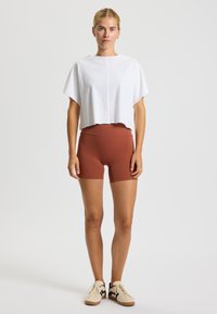 Top corto blanco con mangas cortas combinado con pantalones cortos deportivos de color óxido. La modelo lleva zapatillas beige con detalles en negro.