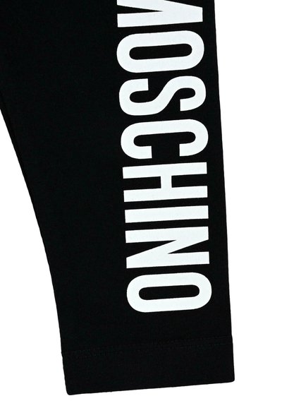 Czarne legginsy z elastycznego materiału bawełnianego, z wyraźnym białym napisem "MOSCHINO" wzdłuż boku. Czyste szwy i brak dodatkowych wzorów.