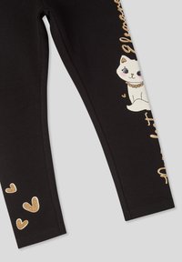 Czarne legginsy z miękkiego materiału z motywem białego kota oraz złotymi akcentami brokatowymi, z małymi złotymi serduszkami nadrukowanymi w pobliżu dołu.