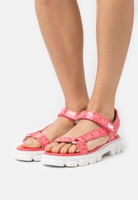 Rosa sportliche Sandalen mit strukturierten Riemen und weißen, klobigen Sohlen. Verfügt über Logodetails und verstellbare Riemen für einen sicheren Sitz.