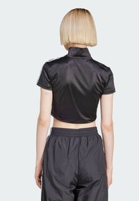 Zwarte korte sportshirt met een opstaande kraag en korte mouwen. Glad oppervlak met witte zijstrepen en gecombineerd met donkere, baggy broeken.