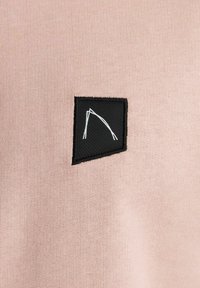 Una tela de color rosa claro presenta un parche rectangular negro con un dibujo a línea blanca, creando un contraste en color y textura.