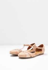Zapatos planos de mujer en color beige con tira en T y hebilla, que presentan una combinación de texturas lisas y de ante en la parte superior.