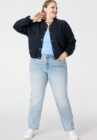 Blouson aviateur à motif marine avec boutons dorés, assorti à un haut bleu clair et un jean droit délavé, baskets blanches.