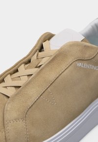 Baskets Valentino en daim beige avec lacets beiges, semelle blanche et nom de la marque visible sur le côté.
