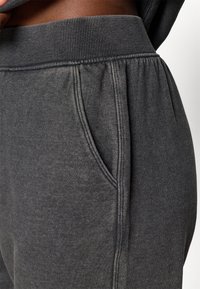 Sive trenerke z rebrastim pasom, elastično teksturo, stranskimi žepi in subtilnimi šivi. Mehka tkanina za udobje.