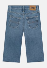 Pantalones cortos de mezclilla con un lavado azul claro, que presentan un diseño de bolsillo trasero cuadrado, costuras doradas y una etiqueta de cuero marrón con el nombre "TOMMY HILFIGER".