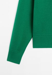 Grøn langærmet sweaterærmekant med ribstrikket detalje på hvid baggrund.