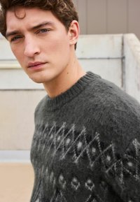 Dark gray knit sweater featuring a geometric pattern with diamonds and lines in lighter shades. Textured fabric with a crew neck design.