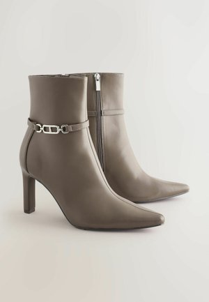 Šedé kožené kotníkové boty s špičatou špičkou, bočním zipem a dekoračním páskem se sponou ve stříbrné barvě. Design na podpatku.