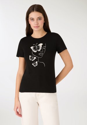Czarny bawełniany t-shirt z białym artystycznym nadrukiem przedstawiającym twarz kobiety i motyle. Okrągły dekolt i krótkie rękawy. Gładkie tło.