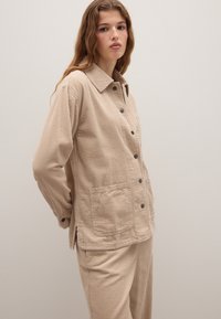 Beige corduroy jacket met een kraag, knoopsluiting, twee opgestikte zakken en ribbelstructuur, gecombineerd met bijpassende broek.