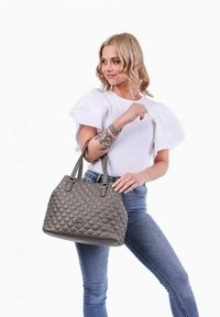 Šedá prošívaná kabelka s hladkými rukojeťmi a kulatým logem jako akcentem. Taška má strukturovaný design a prostorný interiér.
