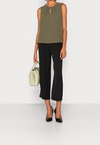 Ärmlös olivgrön topp med en nyckelhålsdetalj, kombinerad med svarta cropped-byxor. Modellen håller en liten ljusgrön handväska och har på sig svarta klackar.