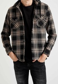 Sort og tan ternet flannel skjorte med hætte, to brystlommer og en sort t-shirt under, parret med mørke jeans.