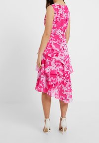 Floral pink dress featuring a tiered design, asymmetrical hem, and sleeveless cut. Made of lightweight fabric with a silky texture.