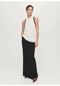 Top blanco sin mangas con cuello alto, combinado con una falda larga negra. Ambas prendas tienen una textura suave y un diseño minimalista. Zapatos marrones.
