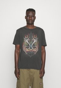 Camiseta de algodón negra con un gráfico frontal de dos serpientes con alas y llamas. Escote redondo y mangas cortas. Ajuste casual.