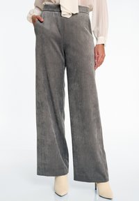 Grijze corduroy wijde broek met verticale ribbels en een elastische tailleband, gepresenteerd met een lichtgekleurde blouse en beige hakken.