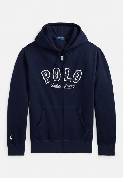 Temno modra jopa z zadrgo, sprednjimi žepi, kapuco z vrvico, napisom "Polo Ralph Lauren" na prsih in majhno belo vezenino logotipa na manšeti levega rokava.