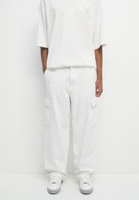 T-shirt blanc oversize et pantalon cargo en tissu léger avec poches latérales. Une paire de baskets blanches complète la tenue.