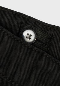 Zwart fabric met een subtiele ribbelstructuur, voorzien van een metalen knoop met vier gaten, bevestigd op een gevouwen stofrand.