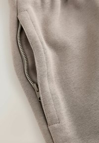 Primo piano di tessuto beige che mostra una cerniera parzialmente aperta cucita nella cucitura di un capo di abbigliamento.